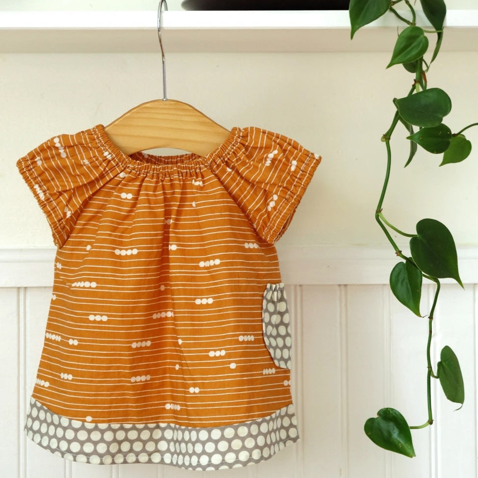 Orange dress with white polka dots on a wooden hanger against a white wall with a plant in the corner.